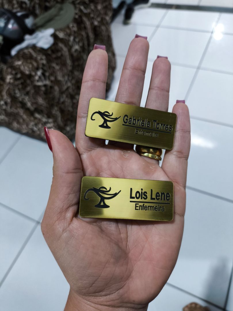 Dois broches personalizados dourados fotografados na mão de uma cliente